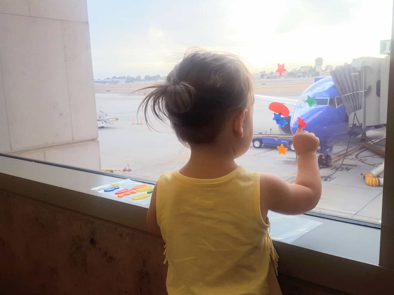 Toddler girl looks out of window at airport.