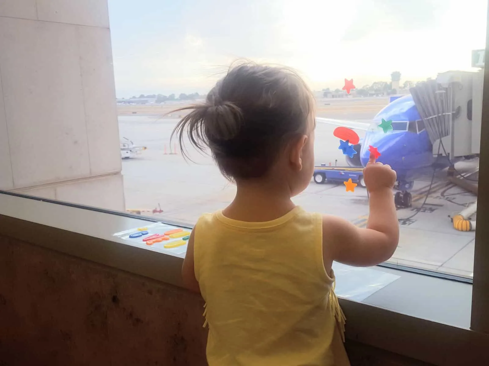 Toddler girl looks out of window at airport.