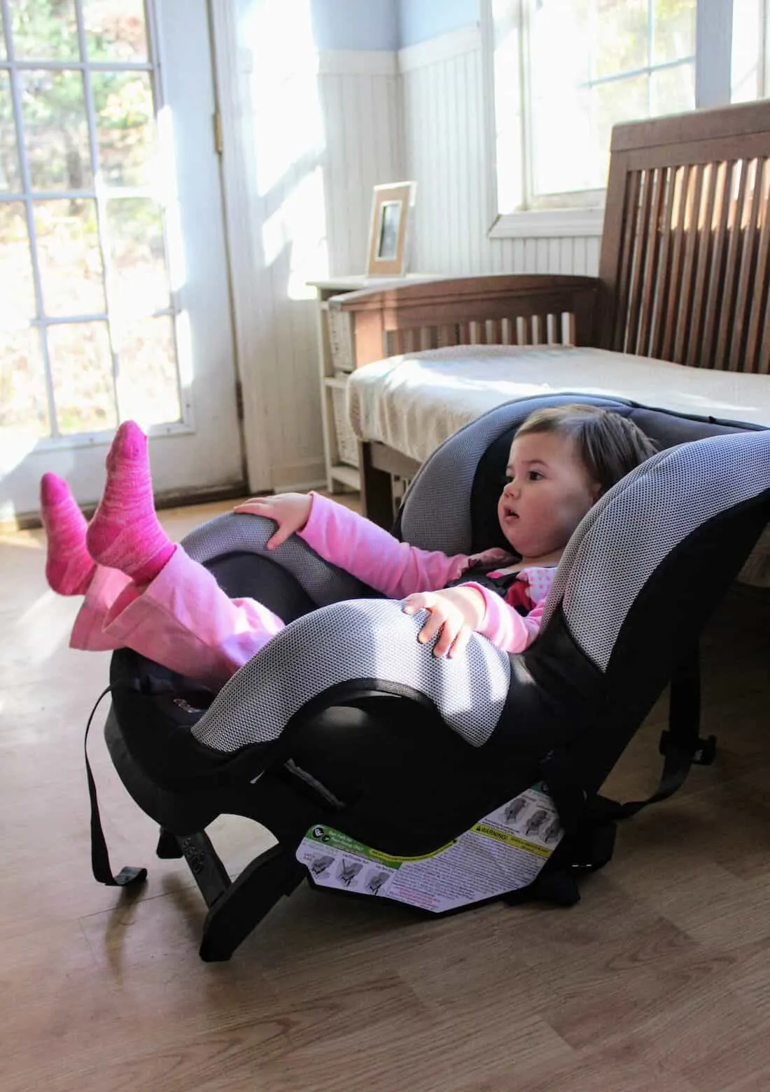 Toddler girl sits in Car Seat inside of house.