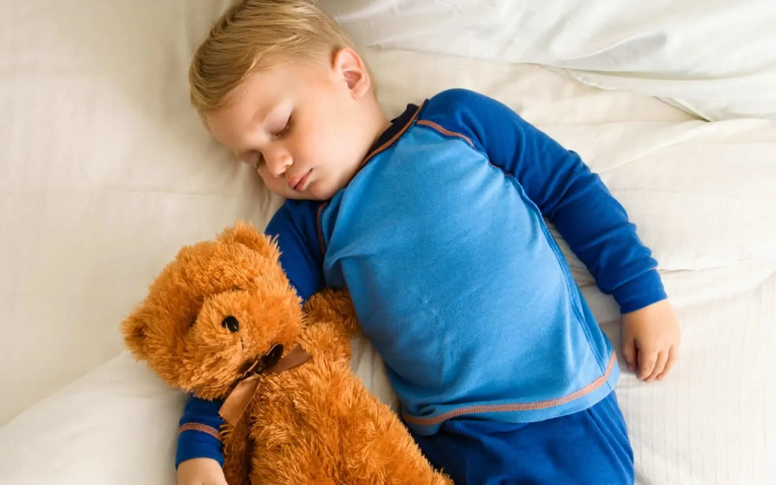 Toddler boy sleeps next to teddy bear.
