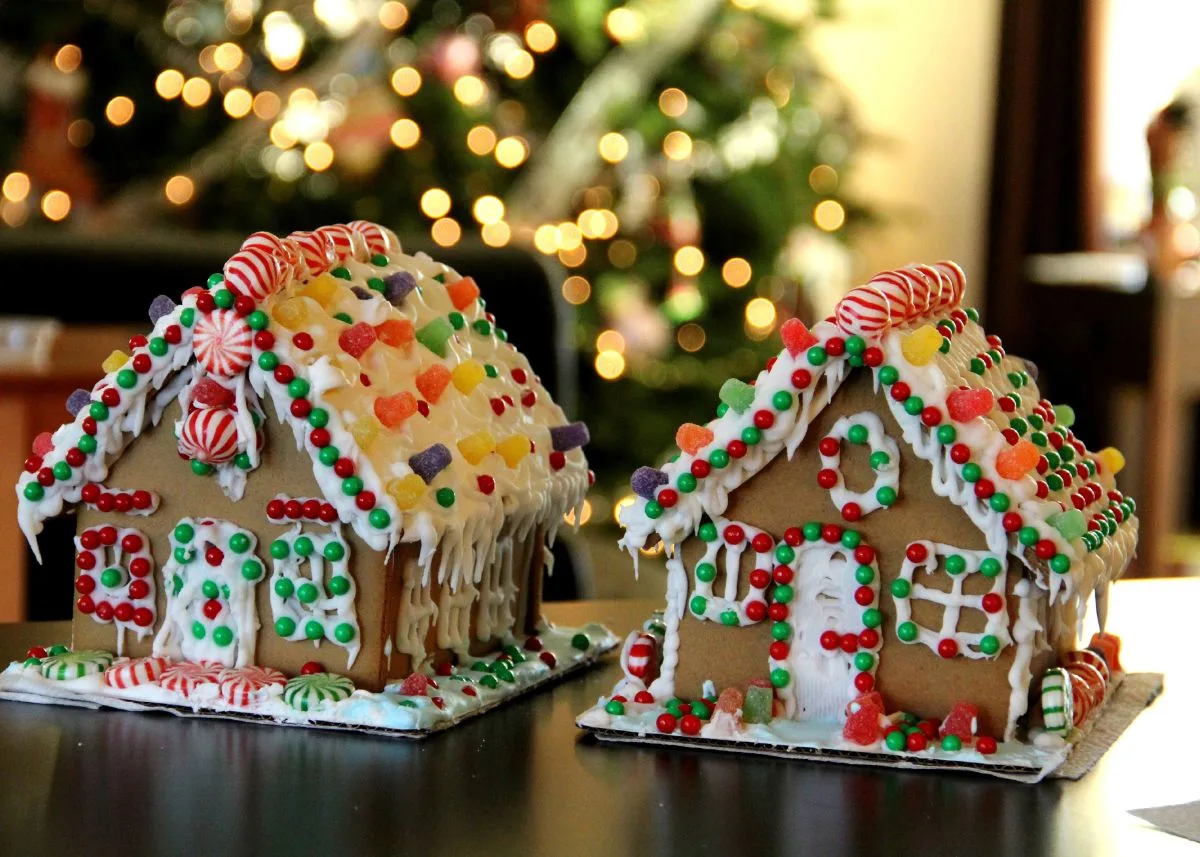 Two decorated gingerbread houses on a table in front of a Christmas tree.