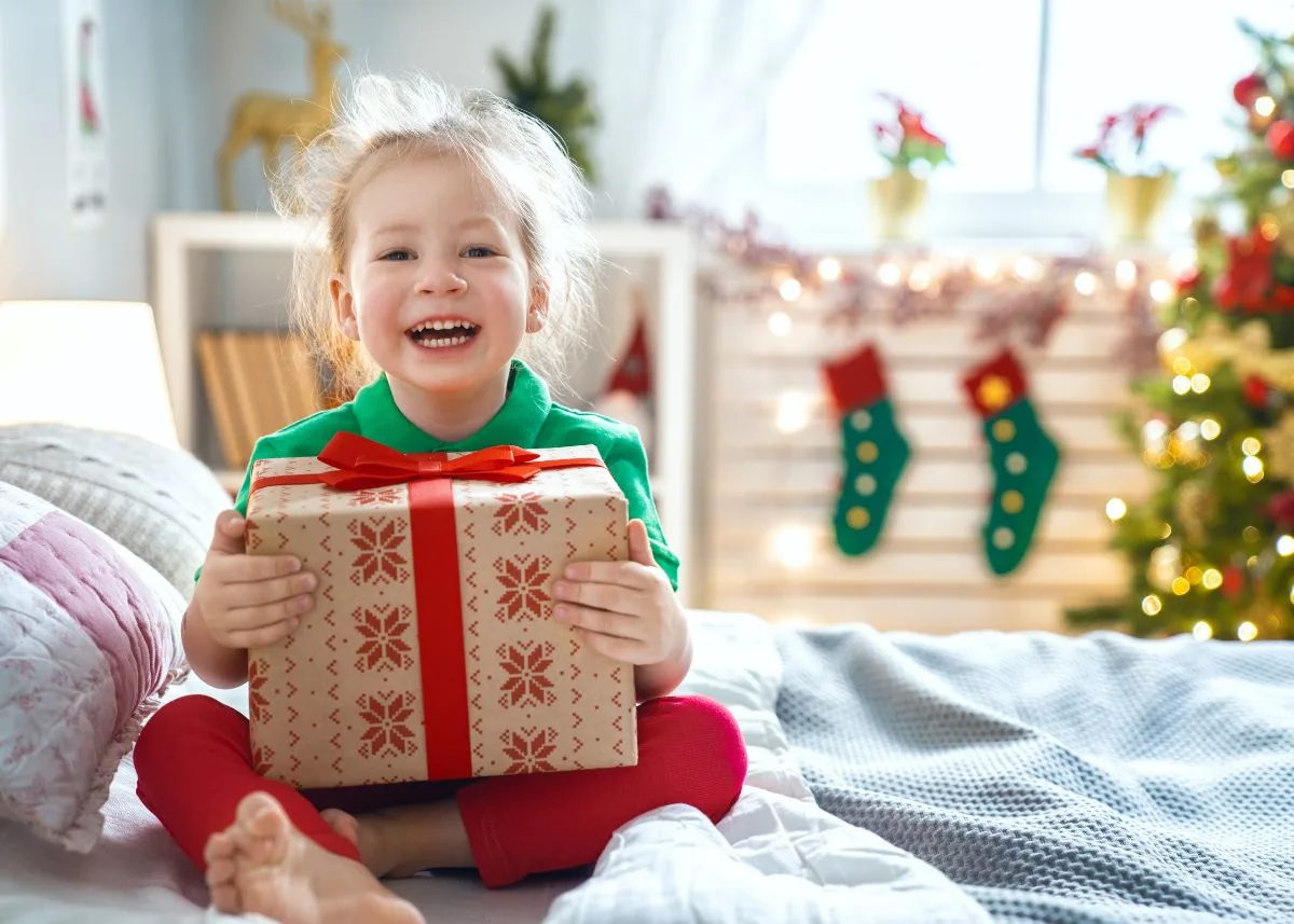 A child with a Christmas present sitting on a bed.
