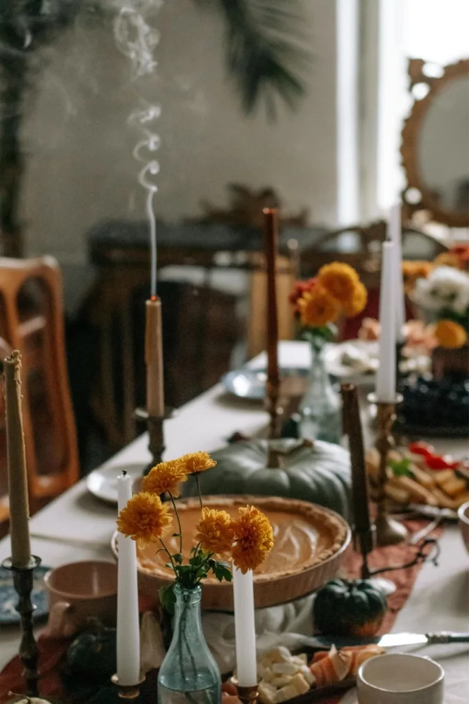 A dining table with green and orange table decor and orange fall flowers.