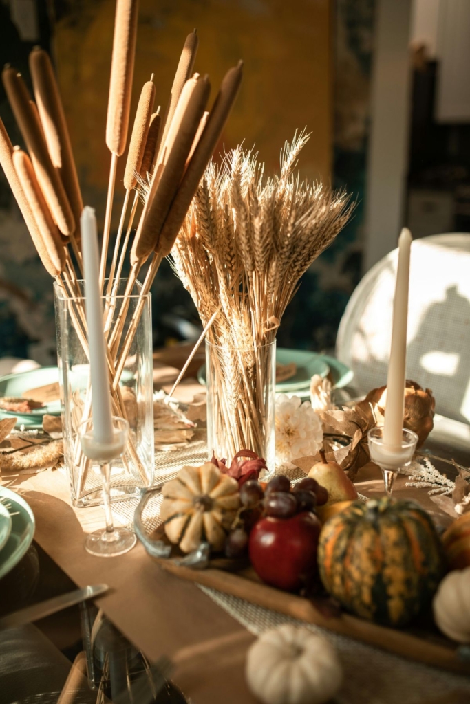 A Thanksgiving table with ornamental grass, pumpkin, and candles.