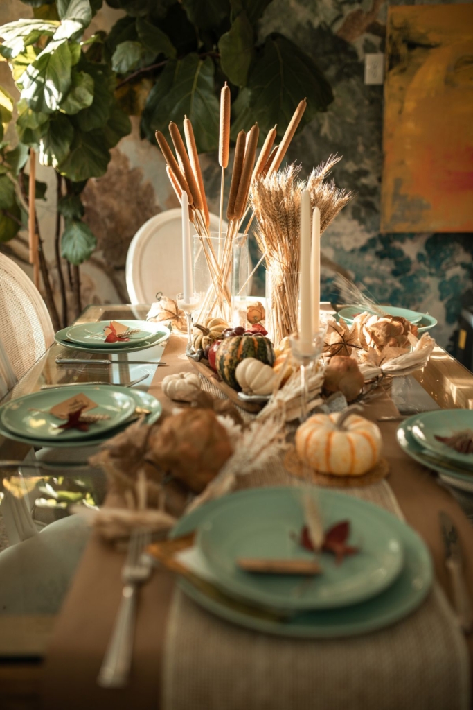 A dining table with green place settings, pumpkins, and ornamental grass.