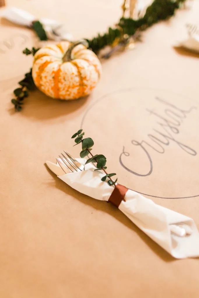 A table covered in butcher paper with drawn on place cards and pumpkin centerpieces.