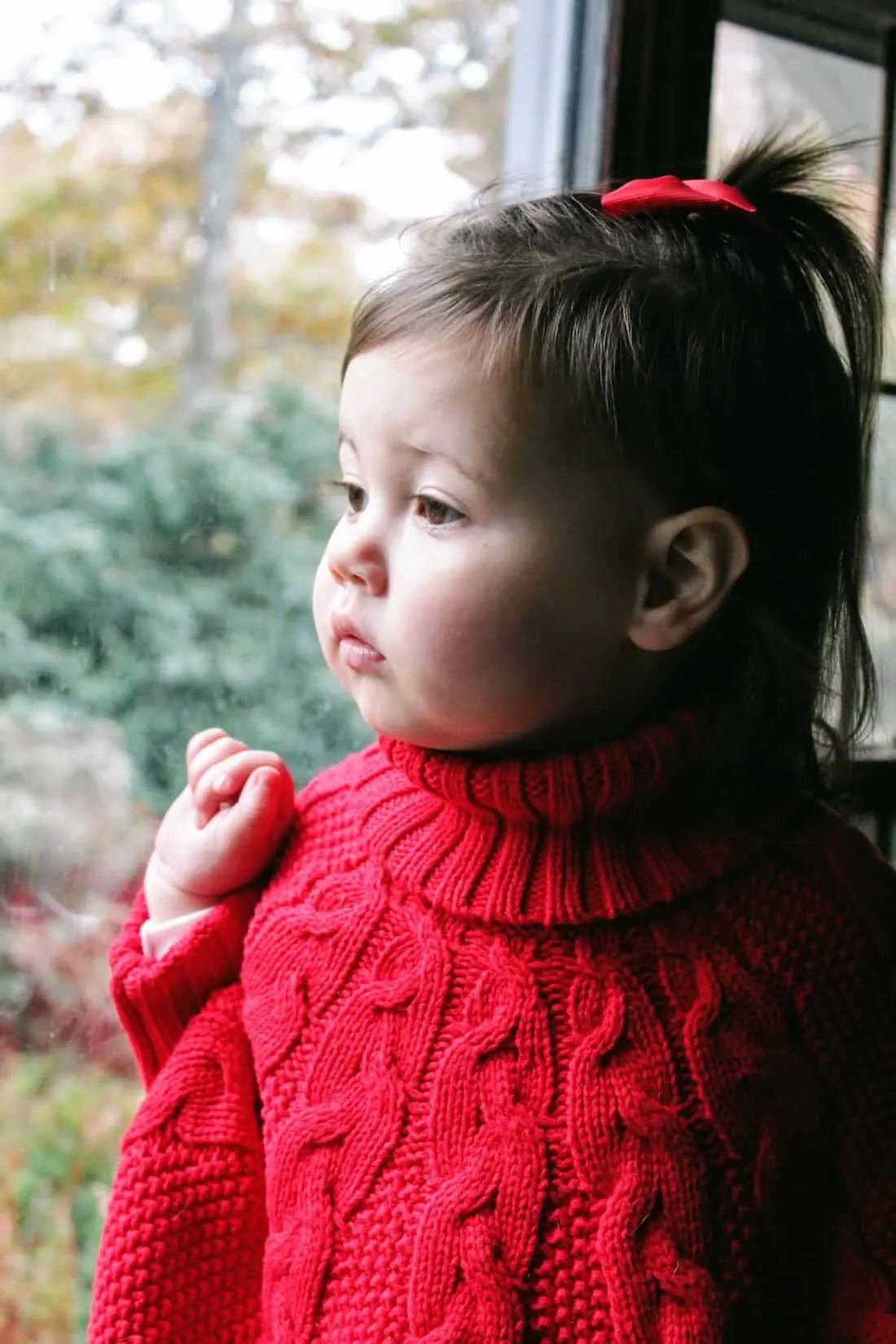 Toddler girl in red Christmas sweeter stares out window.