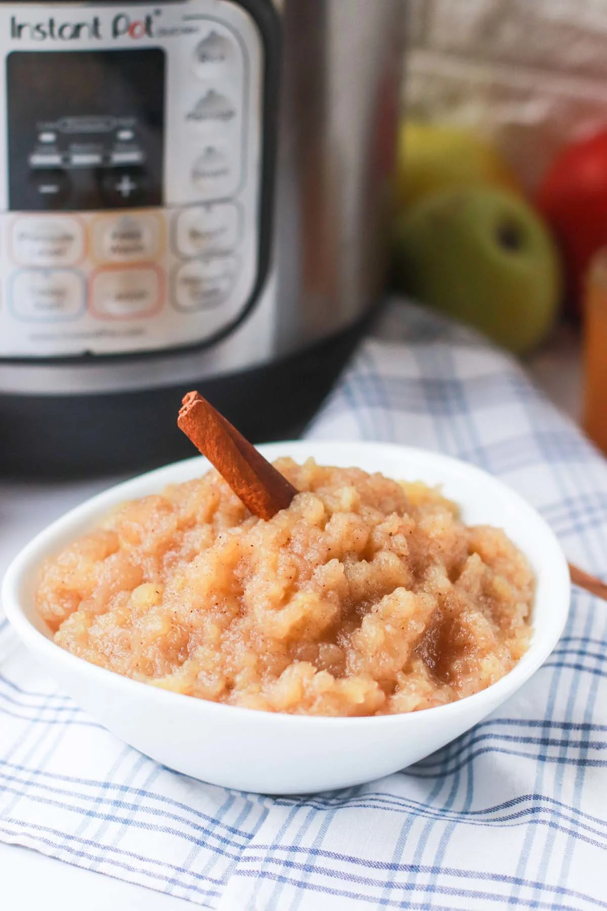 Homemade applesauce in front of an Instant Pot with a cinnamon stick.