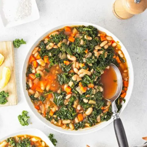 Soup with white beans greens and a tomato broth in a white bowl.