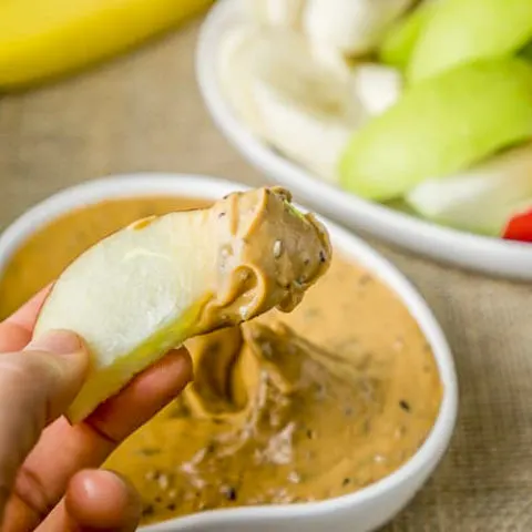 Peanut butter fruit dip and a person dipping a green apple slice.