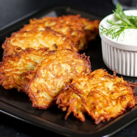 Potato fritters on a black serving plater and a ramekin with white cream and green garnish.
