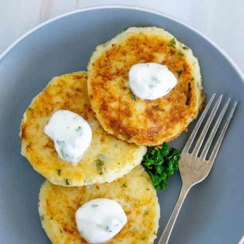 Mashed potatoes fritters on a gray plate with white cream and chives.