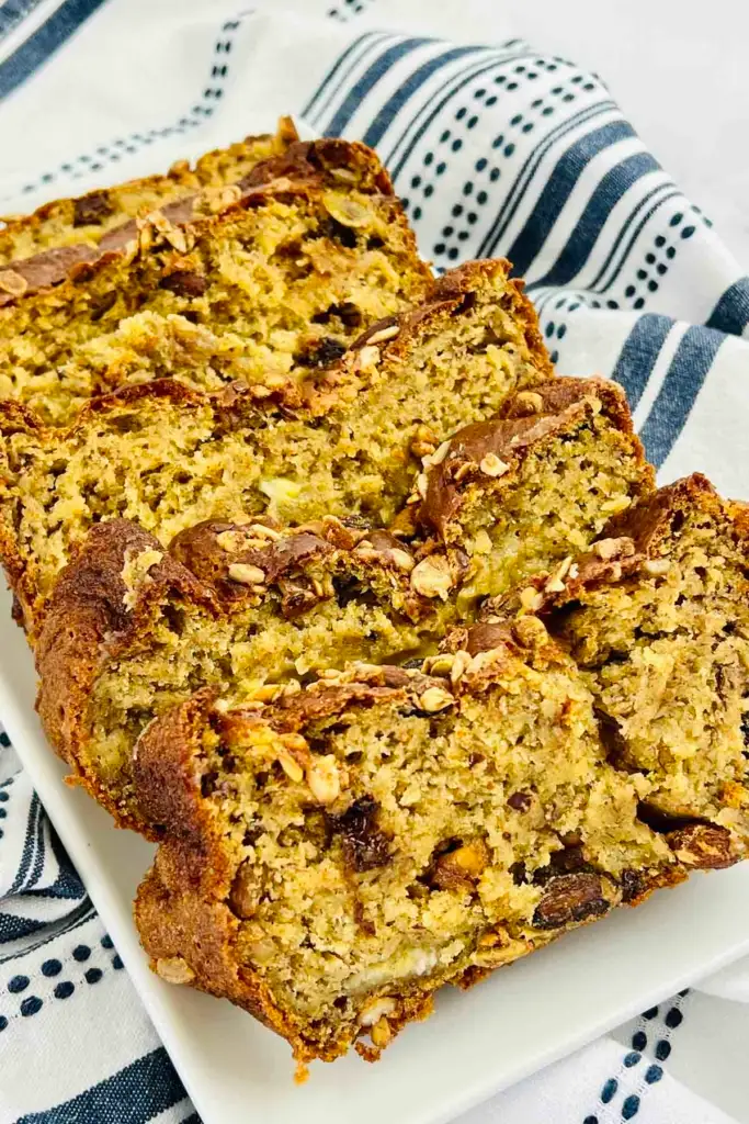 Sliced homemade banana bread with nuts on a white platter over a blue and white striped kitchen towel.