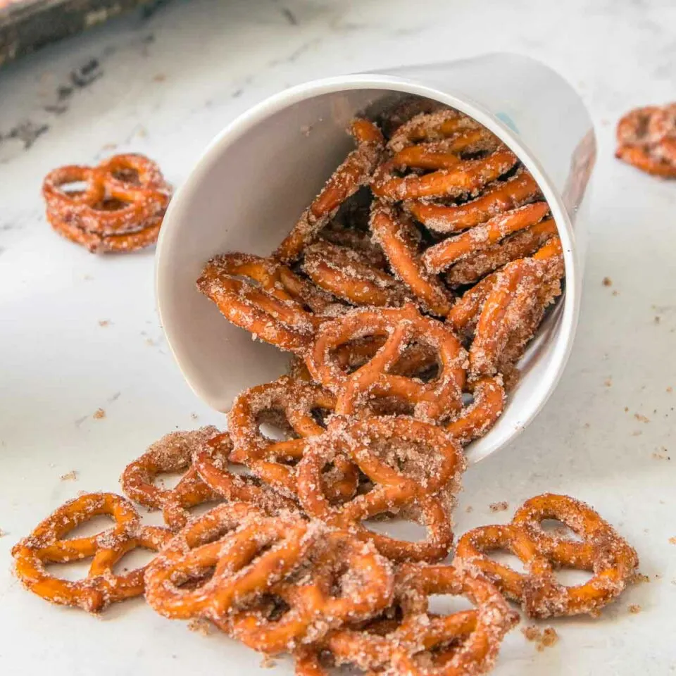 Pretzels spilling from a white cup with sugar and cinnamon on them.