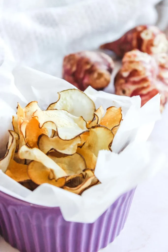Homemade artichoke chips in a purple bowl with white parchment paper.