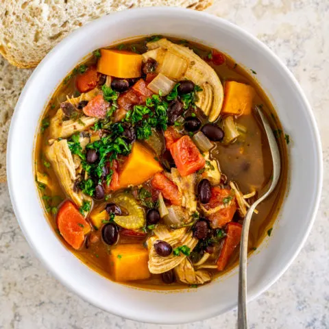 A chicken sweet potato soup with green garnish in a white bowl.