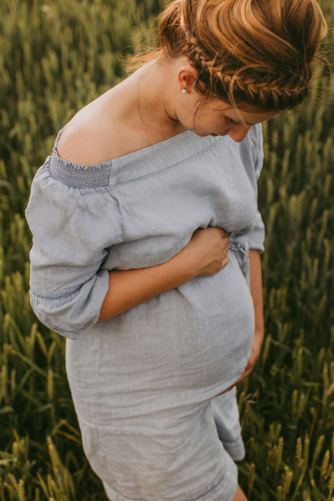 A pregnant woman in a light blue off the shoulder dress outside.