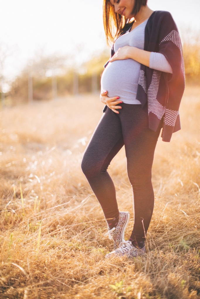 A pregnant woman in black leggings, a gray shirt, and a gray and black sweater.