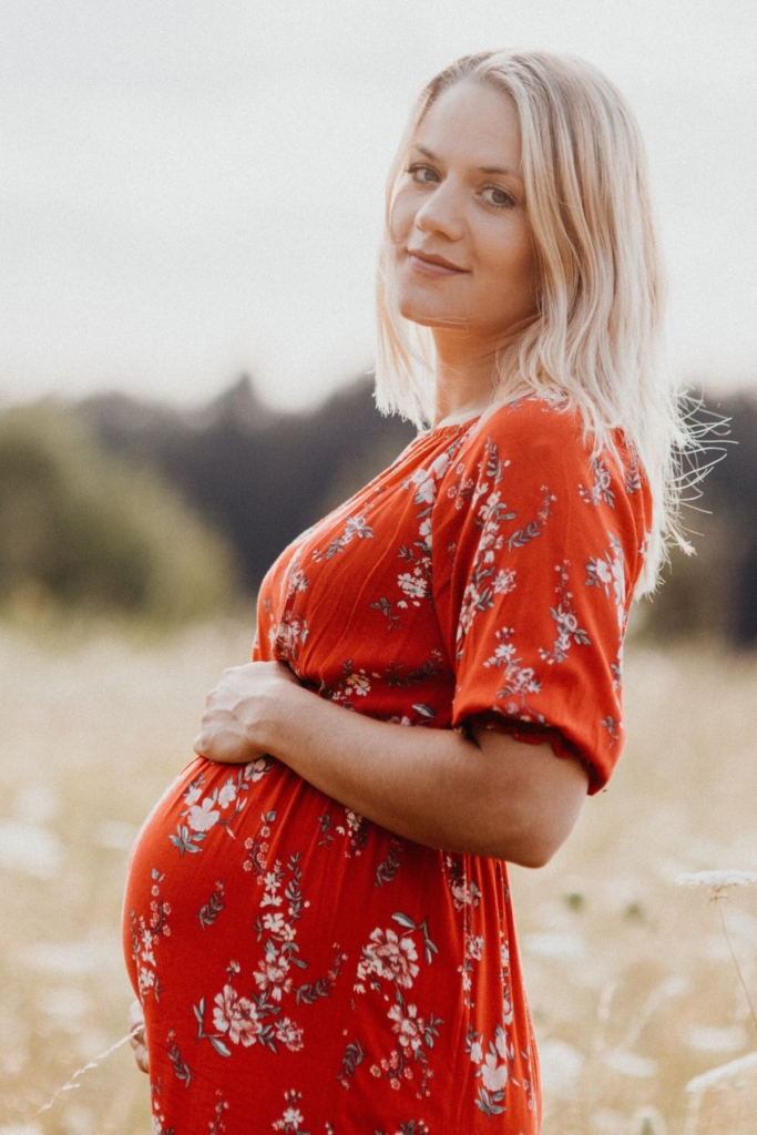 A pregnant woman in a red floral dress outside during fall.