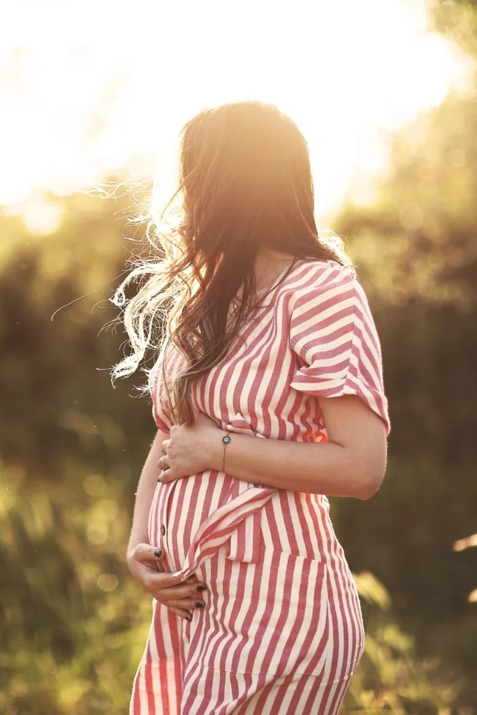 A pregnant woman in a red and white striped dress outside during sunset.