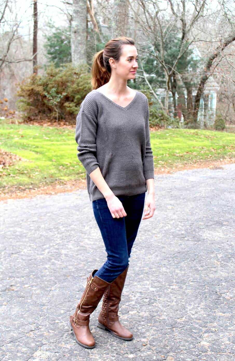 Woman wears grey maternity sweater and brown knee high boots.