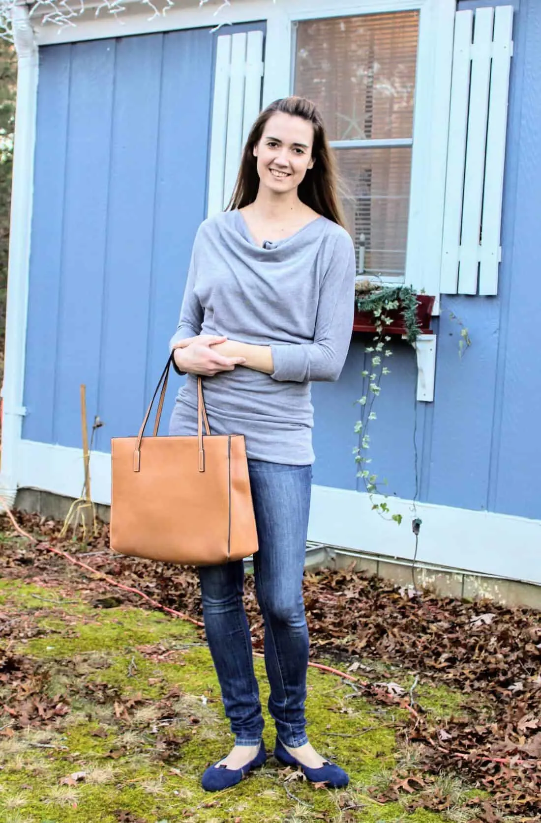 Woman wears grey maternity shirt with camel bag.