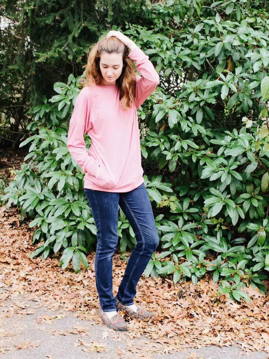 Woman models pink maternity friendly shirt next to wooden area.