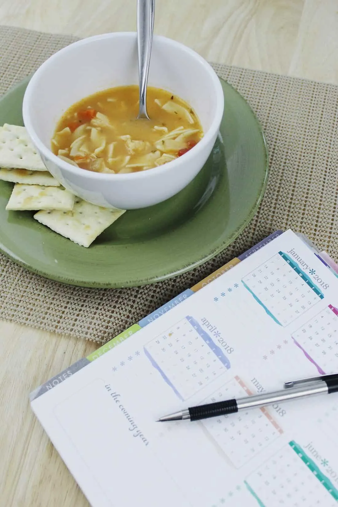Soup and crackers next to planner and pen.