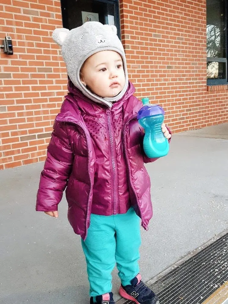 Toddler girl in puffer coat and fuzzy animal hat.