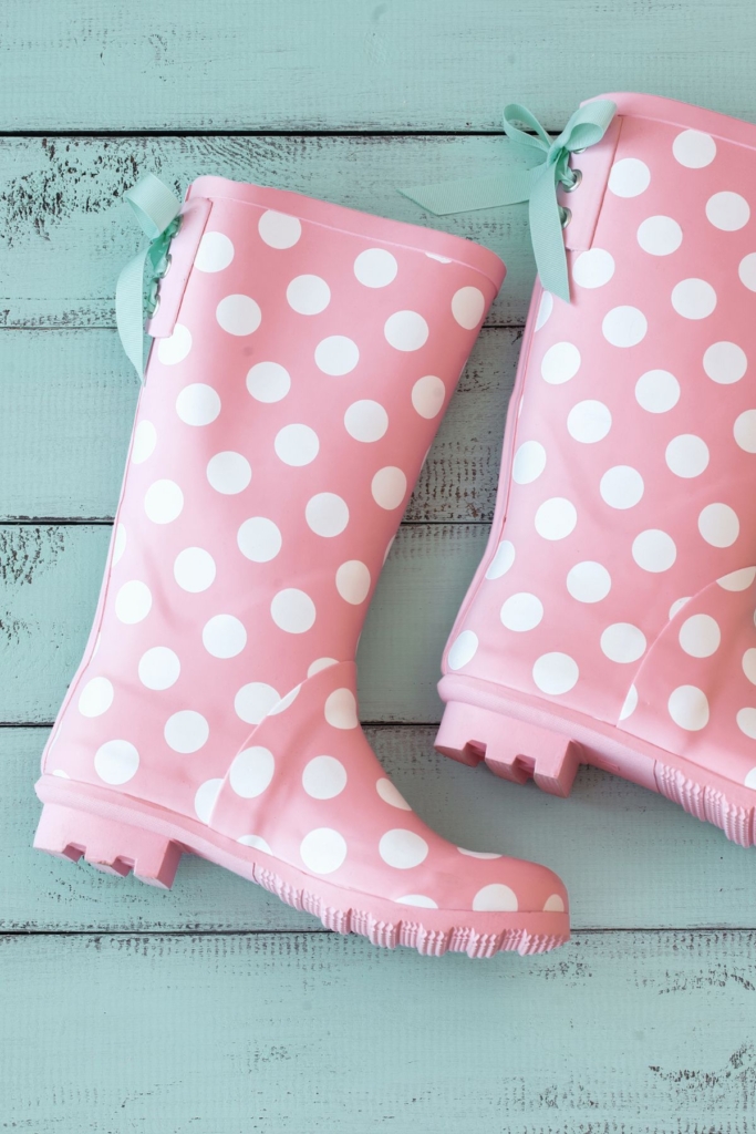 Pink and white polka dot rain boots on a porch.