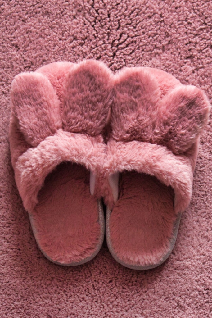 Fluffy pink bunny slippers on a pink carpet.