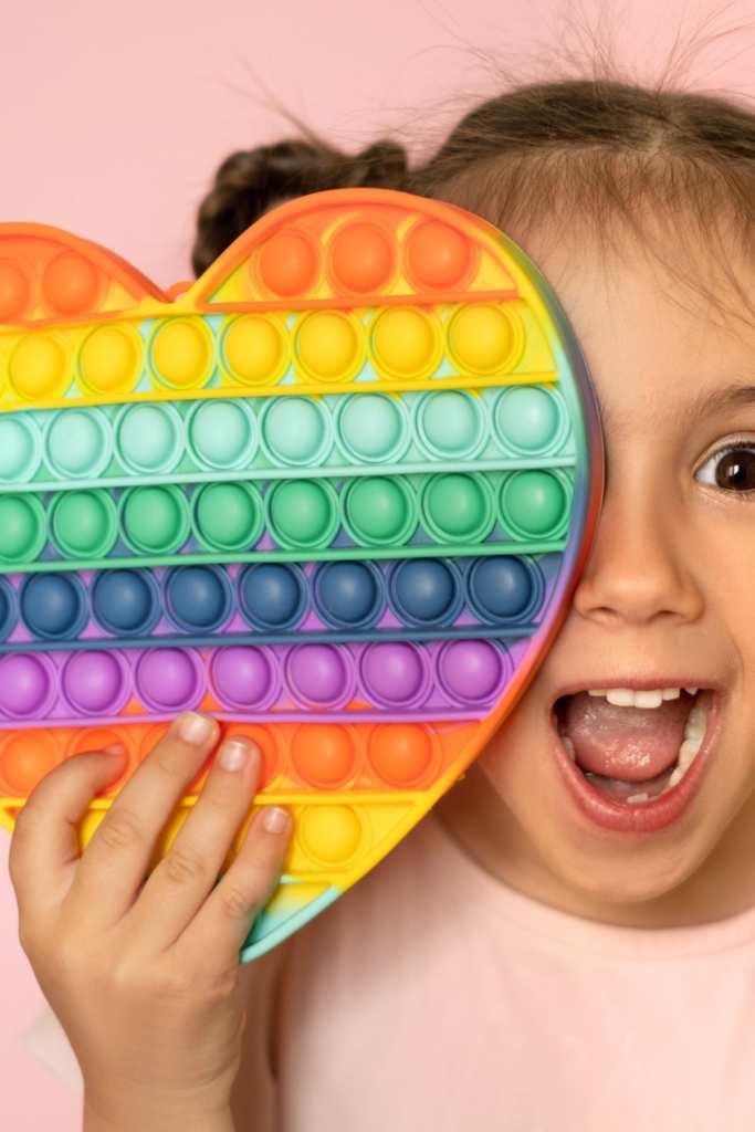 A girl holds a large heart-shaped pop-its toy in front of her face.