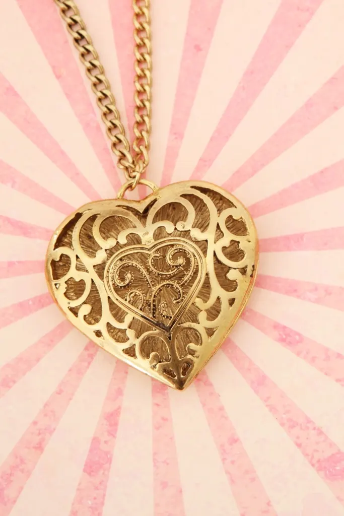 An ornate heart-shaped gold locket on a pink starburst background.
