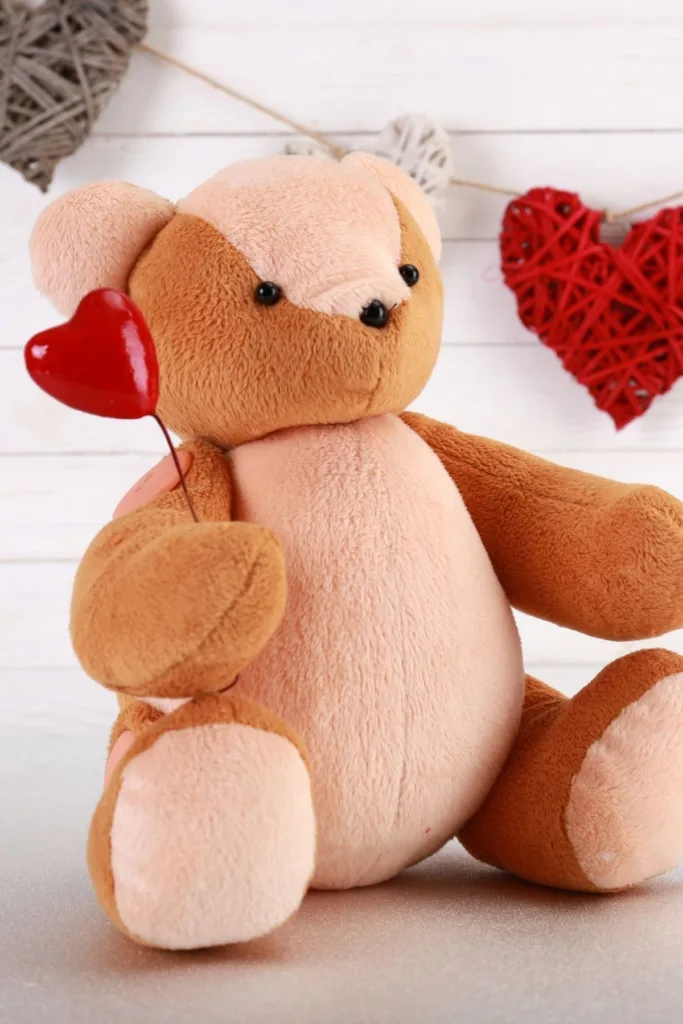A teddy bear holding a heart in front of a Valentine's Day garland.