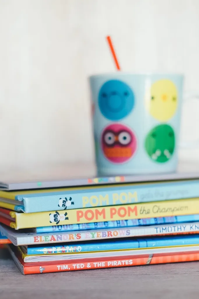 A stack of children's books and a cup on a table.