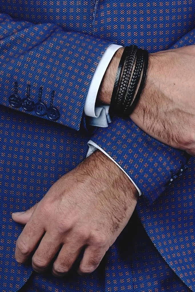A man in a blue business suit shows off his leather bracelets.