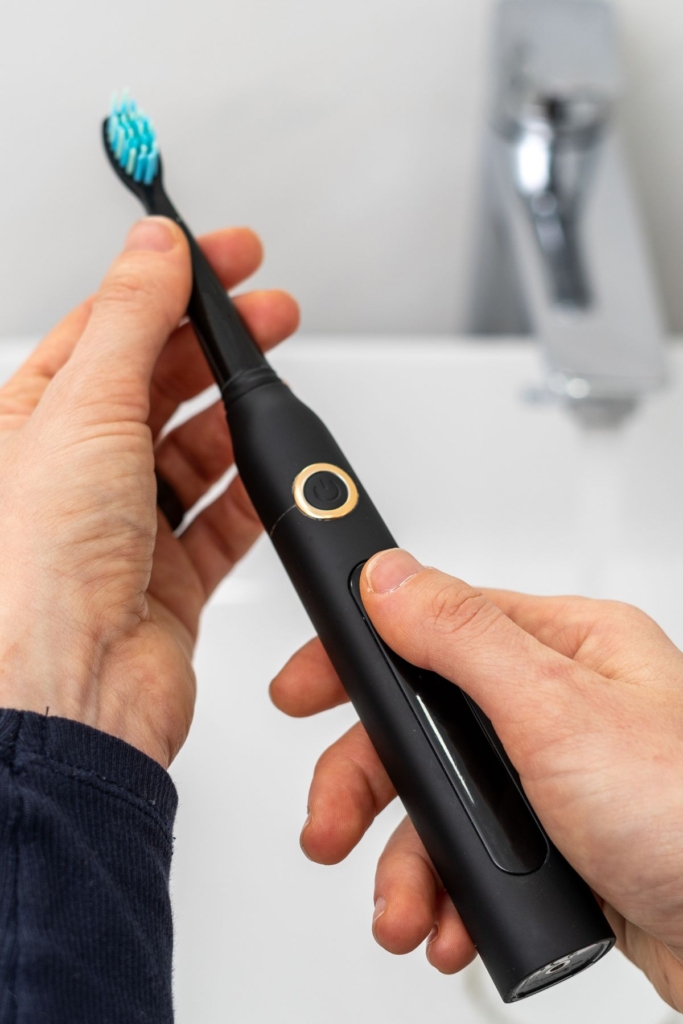 A man holds a black electric toothbrush next to a sink.