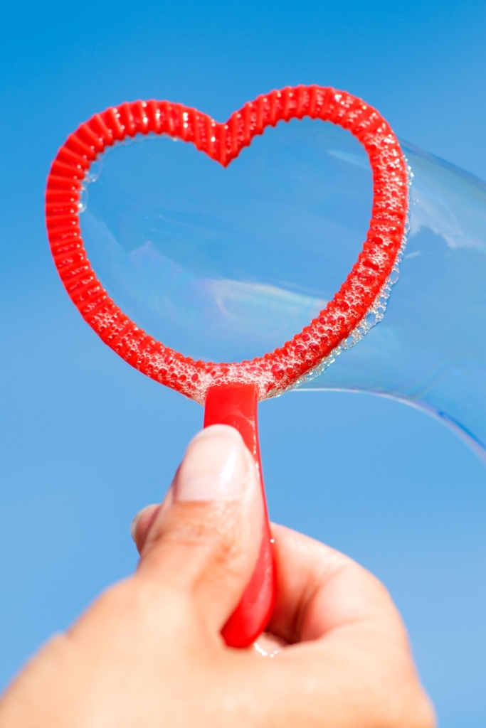 A red heart-shaped bubble wand with bubbles blowing out.
