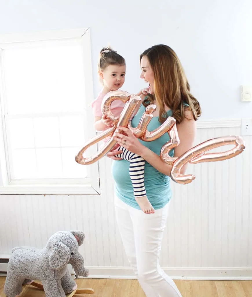 Woman holds pink girl balloon to announce her baby's gender.