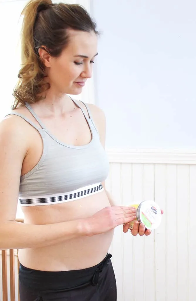 Pregnant woman holds container of stretch mark cream.