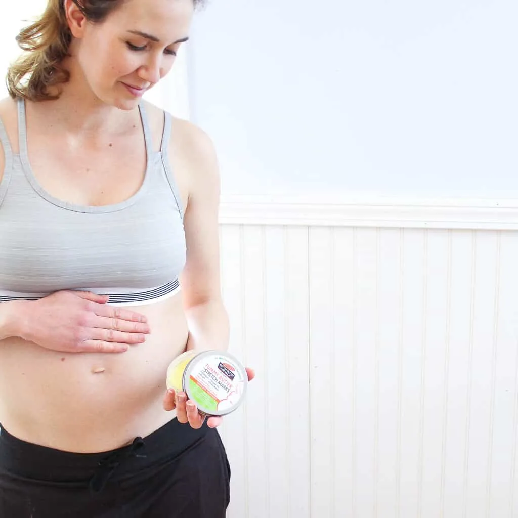 Woman massages stretch mark cream onto pregnant belly.