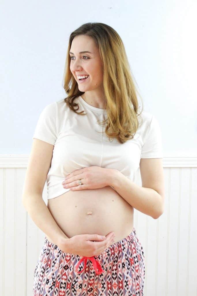 Pregnant woman holds belly and looks away from camera.