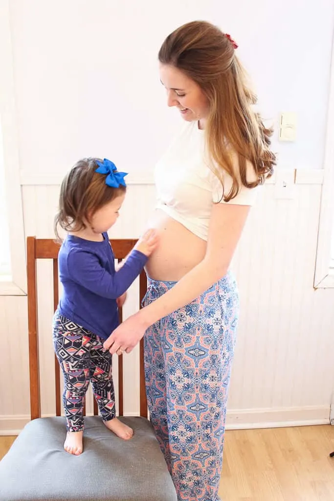 Toddler girl places hand on her mother\'s pregnant belly.