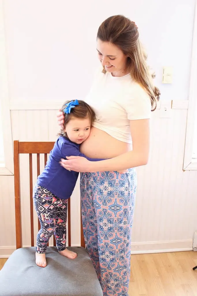 Toddler girl hugs her mother\'s pregnant belly.