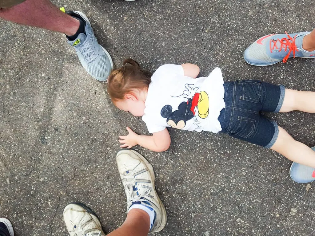 Toddler girl lays on the ground surrounded by family at Disney park.