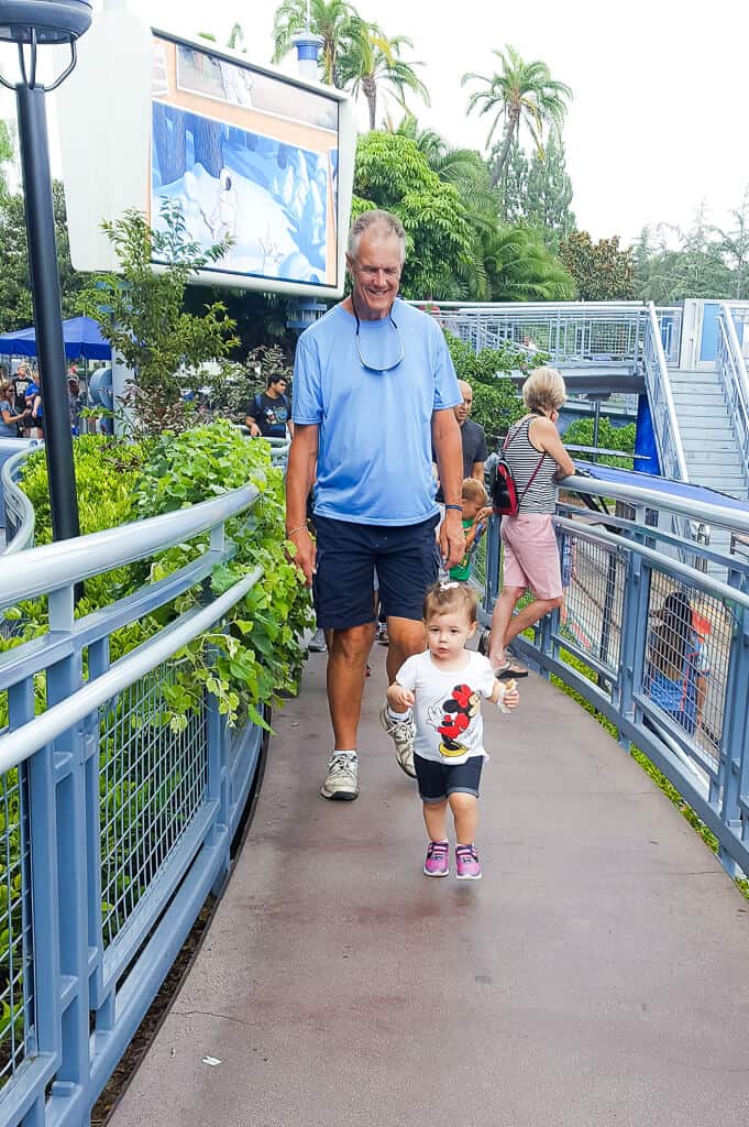 Toddler girl walks through Disney Park with Grandfather.