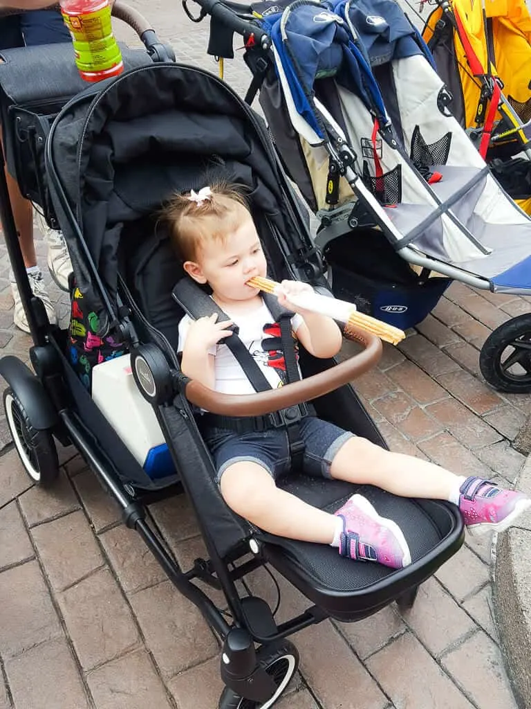 Toddler eats snack in stroller at Disney.