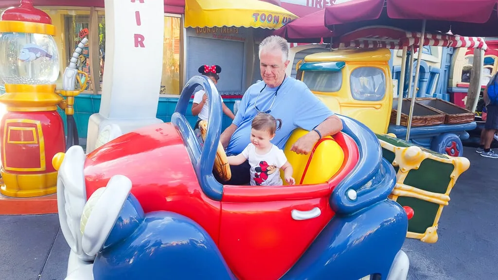 Man sits on Disney ride with granddaughter.