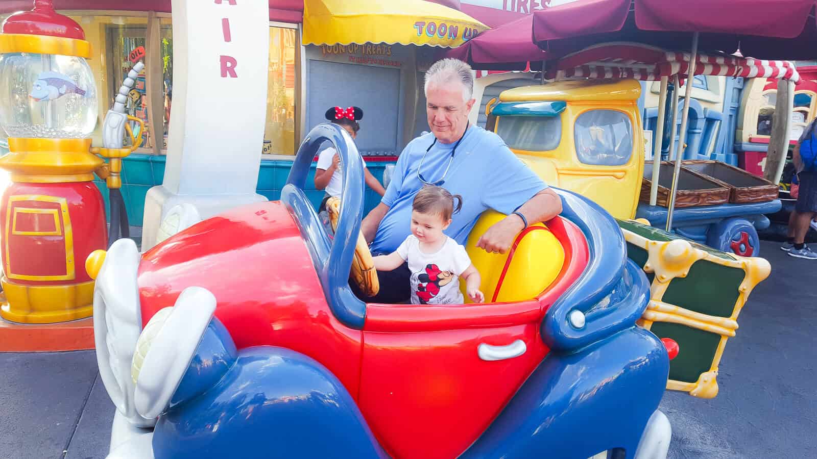 Toddler girl and grandfather on ride at Disney.