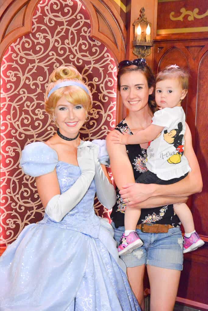 Mother poses with Toddler girl and Disney princess at Disney park.